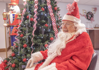 Senior man in Santa suit poses next to Christmas tree